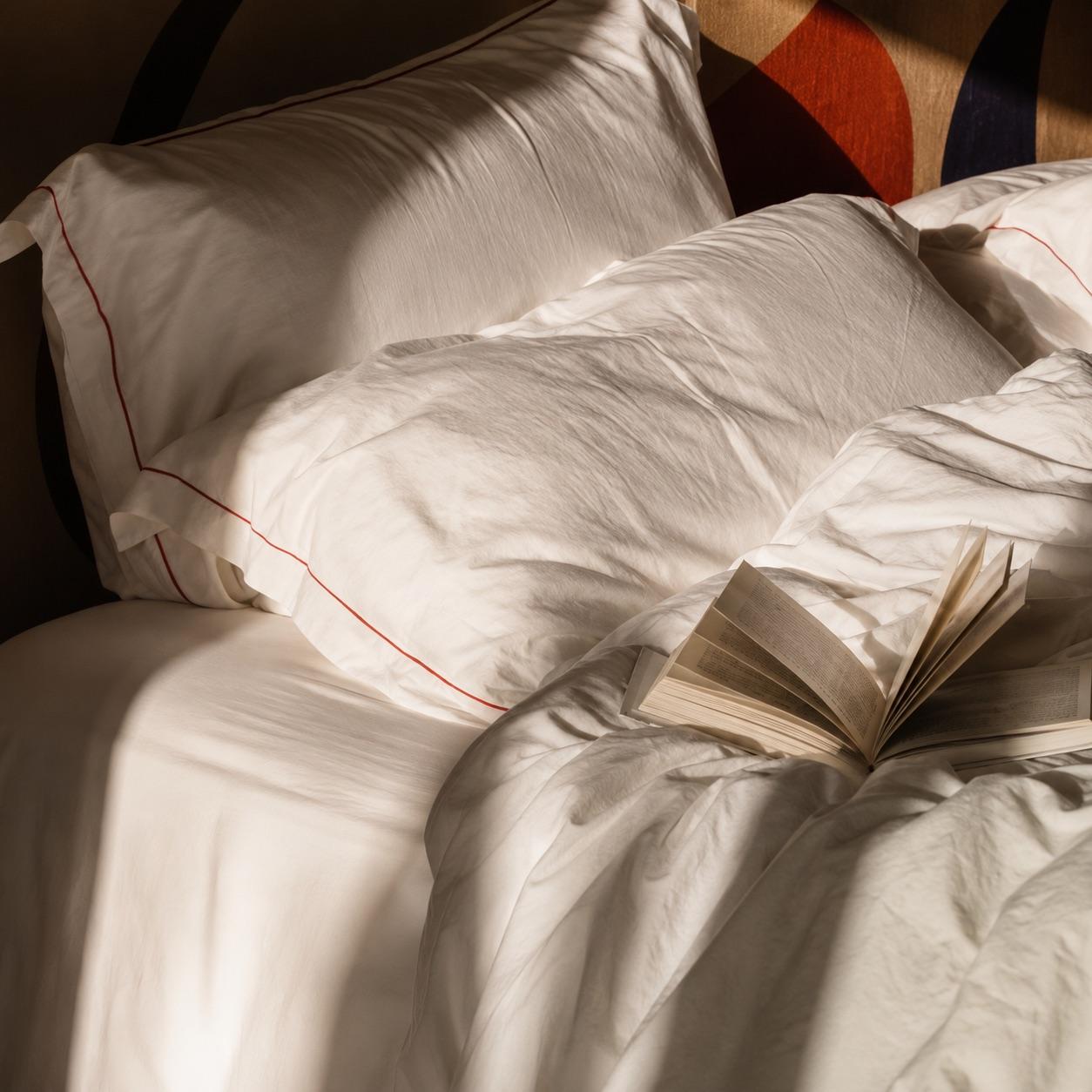 An unmade bed at first light, a book left open on the covers
